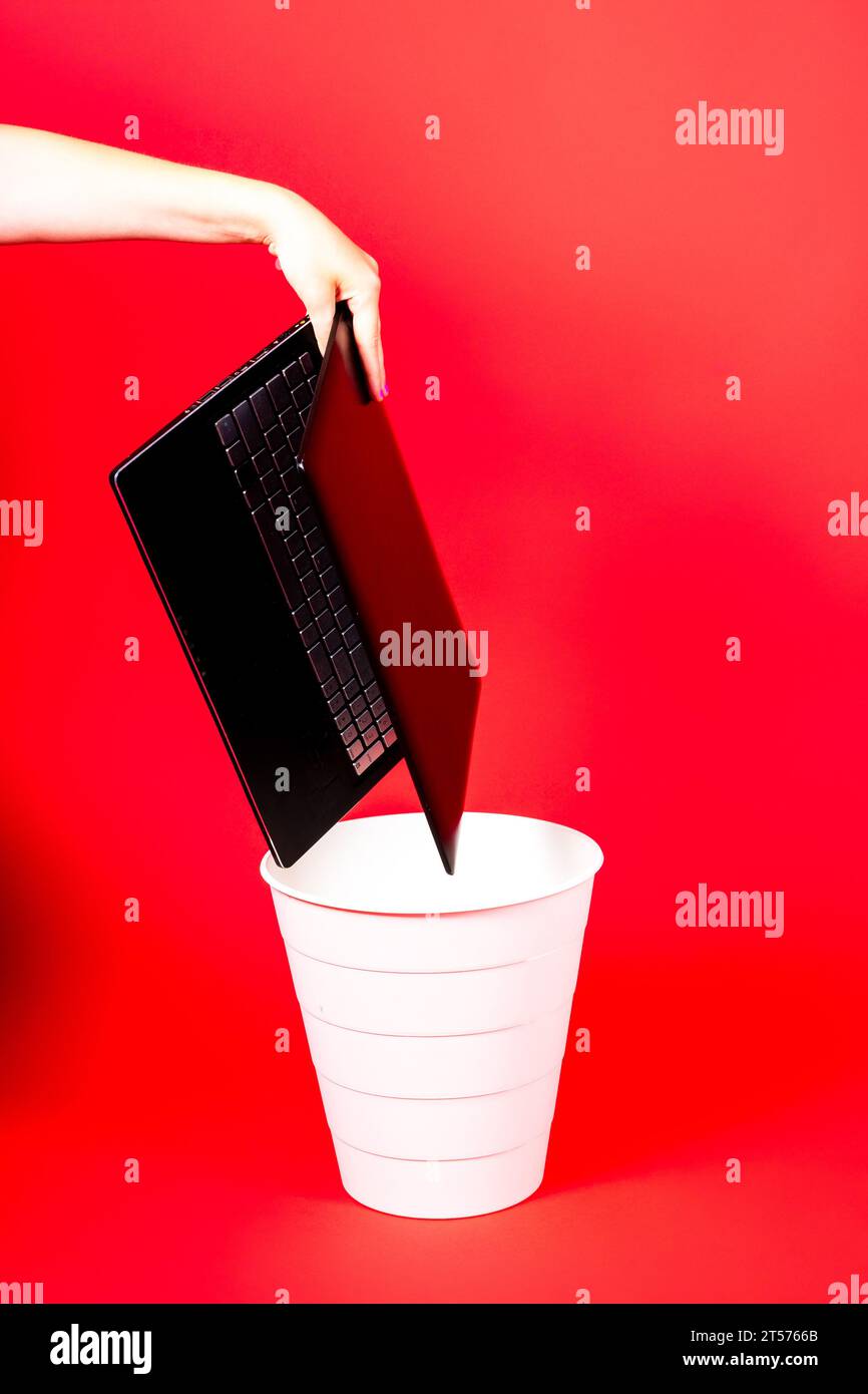 Schwarzer Laptop in einem Papierkorb auf rotem Hintergrund isoliert Stockfoto