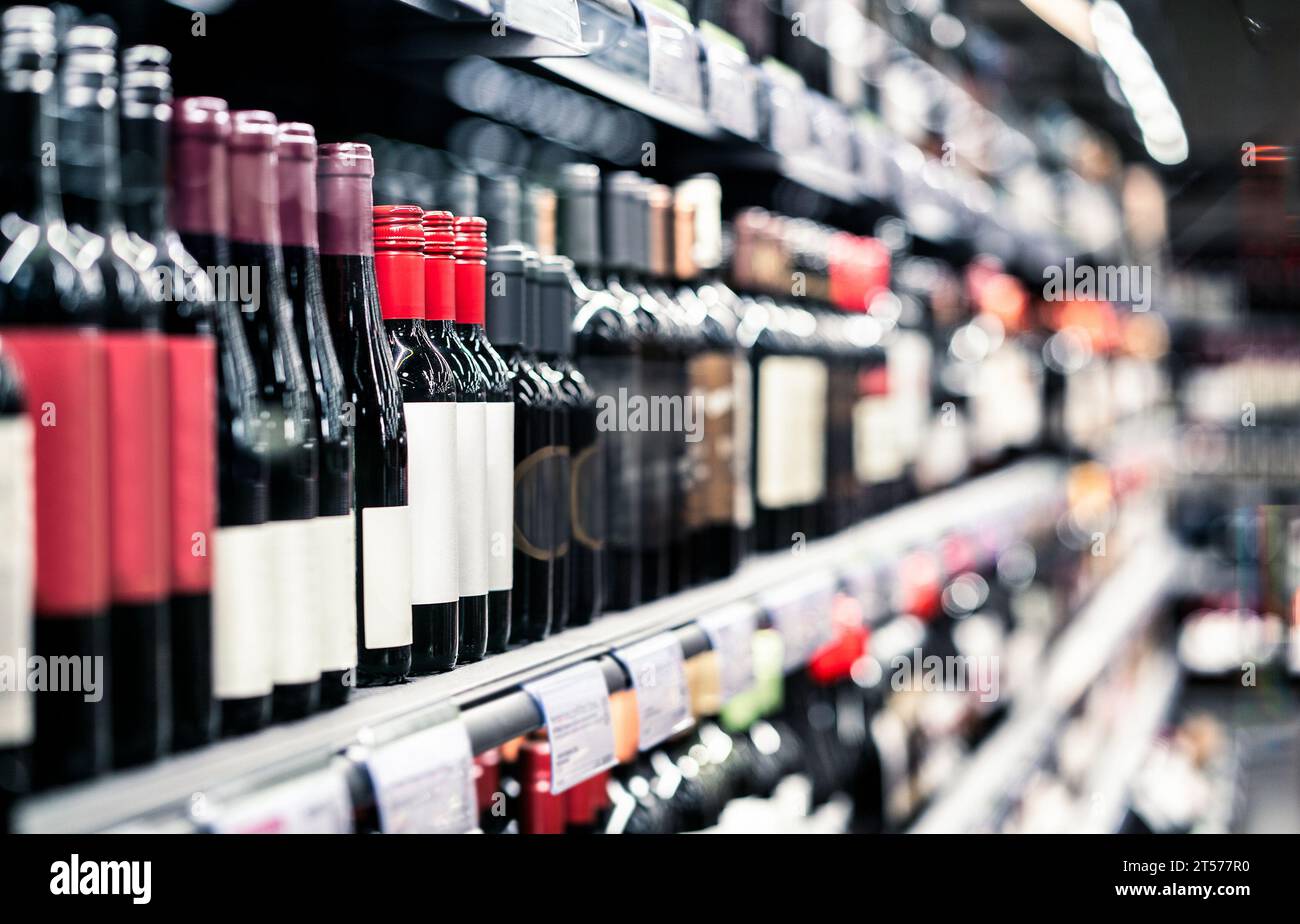 Spirituosengeschäft, Spirituosengeschäft. Rotwein auf dem Regal. Konzentrieren Sie sich auf Flaschen, Supermarktgang im Hintergrund. Verkauf von alkoholischen Getränken und Auswahl im Lebensmittelmarkt. Stockfoto