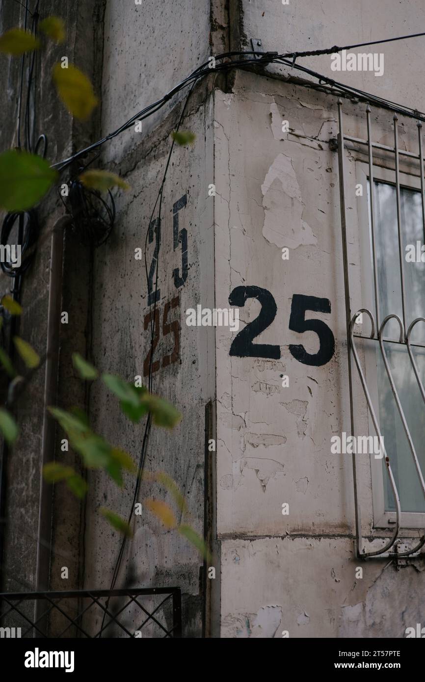 Die Zahl fünfundzwanzig ist dreimal mit einer Schablone auf eine graue Wand an der Ecke des Hauses gemalt, nahe Fenster mit Gittern. Hausnummer 25. Stockfoto