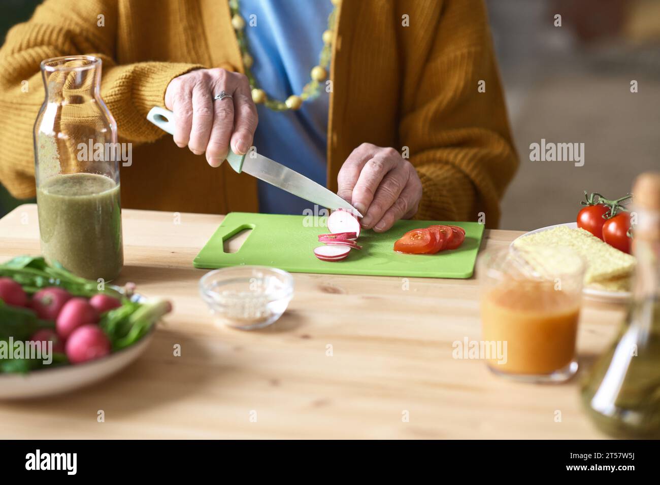 Nahaufnahme einer Seniorin, die Gemüse für Salat auf Schneidebrett am Tisch schneidet Stockfoto