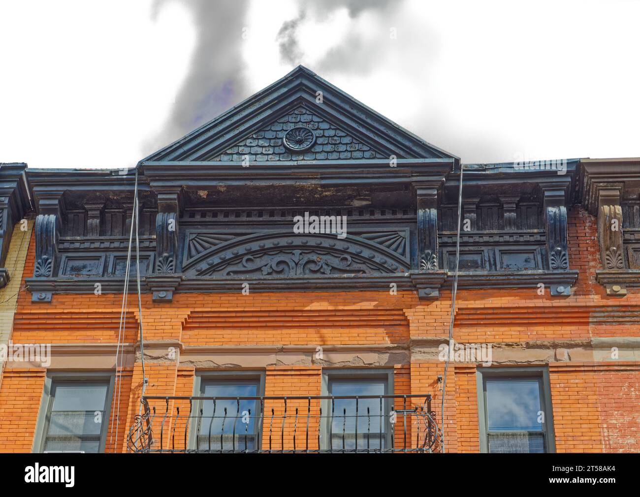 Ein gemaltes, gestanztes Metallgesims setzt die Dachlinie der 521 East 83rd Street ein; darunter sind Sandsteinstürze zerbröckeln. Stockfoto