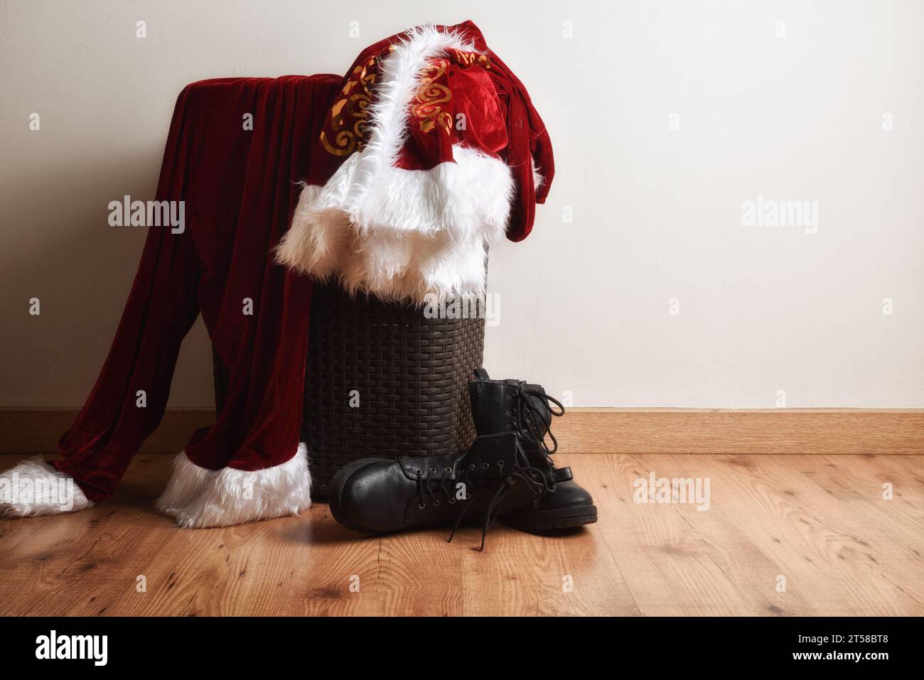 weihnachtsmann-Anzug auf Kleiderkorb im Zimmer mit Holzboden und weißer Wand dahinter. Stockfoto