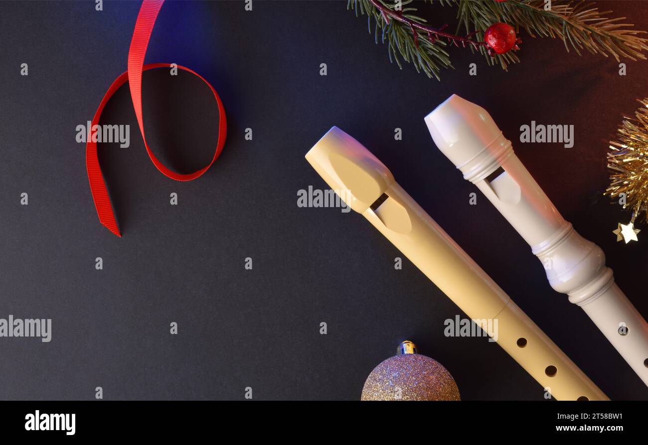 Zwei traditionelle Kunststoffrecorder für Kindermusik auf einem schwarzen Tisch mit Weihnachtsdekoration. Draufsicht. Stockfoto