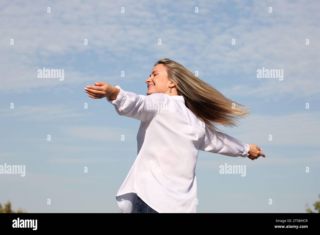 AUSDRÜCKE VON GLÜCK UND WOHLBEFINDEN VON EINEM BLONDEN MÄDCHEN IN WEISSEM HEMD MIT BLAUEM HIMMEL IM HINTERGRUND Stockfoto