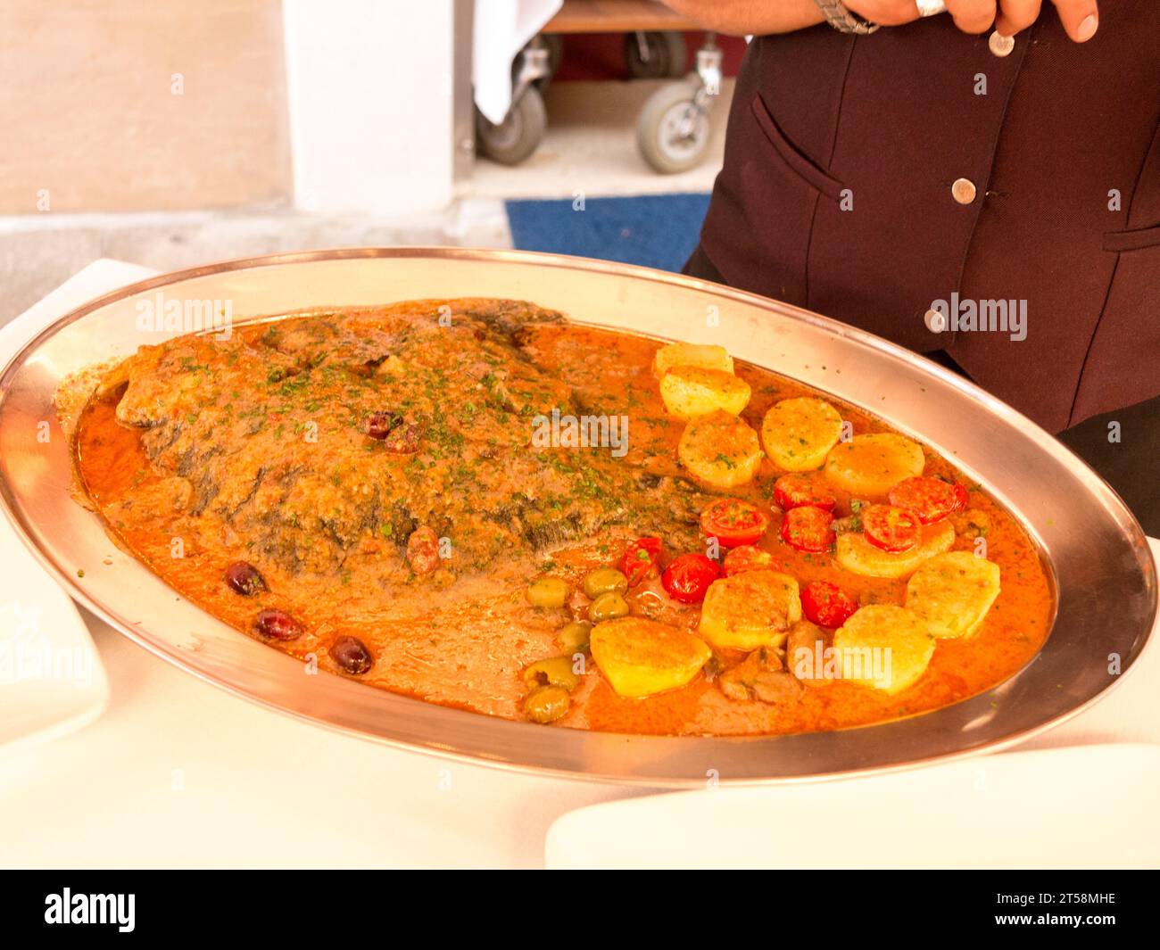 Fischgericht im Restaurant Alla Conchiglia in Venedig, Italien. Der Fisch wird in einer Spinat- und Tomatensauce gebadet, dazu Kartoffeln und kleine Tomaten Stockfoto