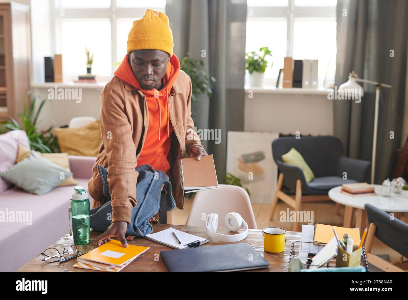 Horizontale Aufnahme eines modernen afroamerikanischen College-Studenten, der am Schreibtisch steht und sich auf die Schule vorbereitet, indem er Lehrbücher und Copybooks in den Rucksack packt Stockfoto
