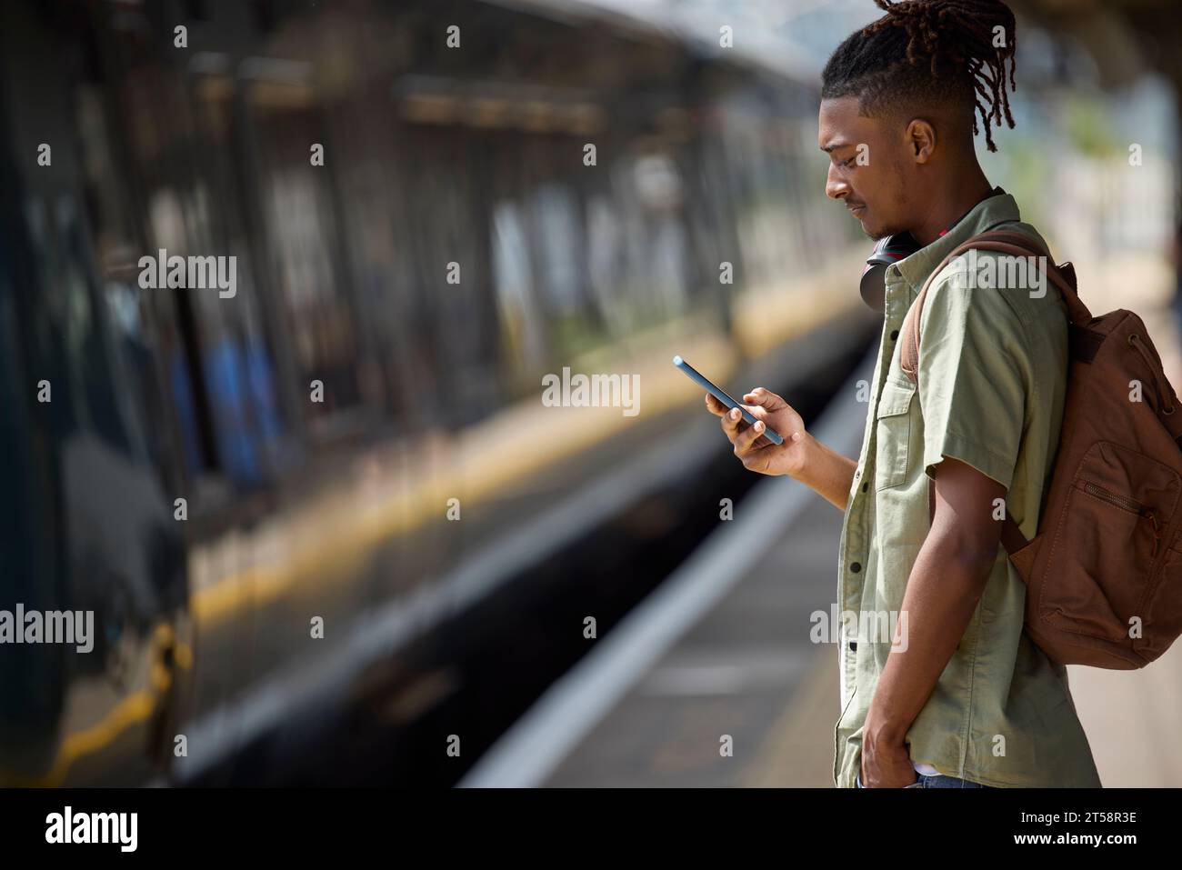 Junger Mann Pendelt Auf Dem Zug Zur Arbeit, Steht Auf Dem Bahnsteig Und Sieht Sich Das Handy An, Wenn Der Zug Kommt Stockfoto