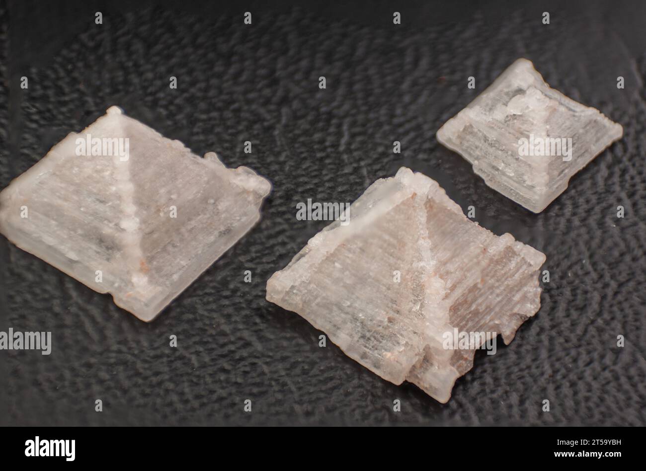 Nahaufnahme von drei Pyramidensalzkristallen auf dunklem, strukturiertem Hintergrund. Stockfoto