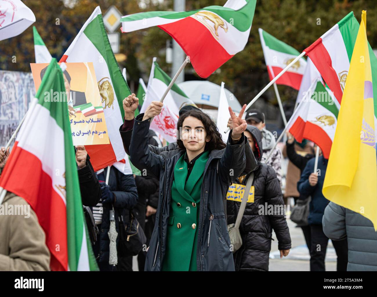 Genf, Schweiz. November 2023. Eine junge Frau schwenkt die dreifarbige iranische Flagge mit dem Aufdruck Löwe und Sonne, während andere im Hintergrund das Emblem der wichtigsten iranischen Oppositionsgruppe, der Mudschahedin-e Khlaq (PMOI/MEK), während der Kundgebung im Palais des Nations tragen. vor dem Europäischen Hauptquartier der Vereinten Nationen, um gegen die Ernennung des iranischen Regimegesandten zum Vorsitzenden des Sozialforums des UN-Menschenrechtsrates zu protestieren. Quelle: SOPA Images Limited/Alamy Live News Stockfoto