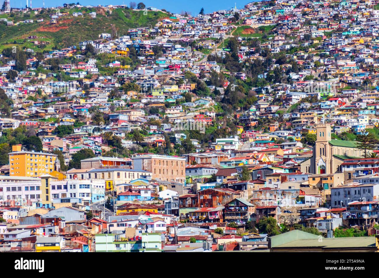 Buntes Stadtbild mit Häusern in Valparaiso, Chile. Die Gebäude sind eng zusammengesetzt und breiten sich in der Wintersonne den Hang hinauf aus. Stockfoto