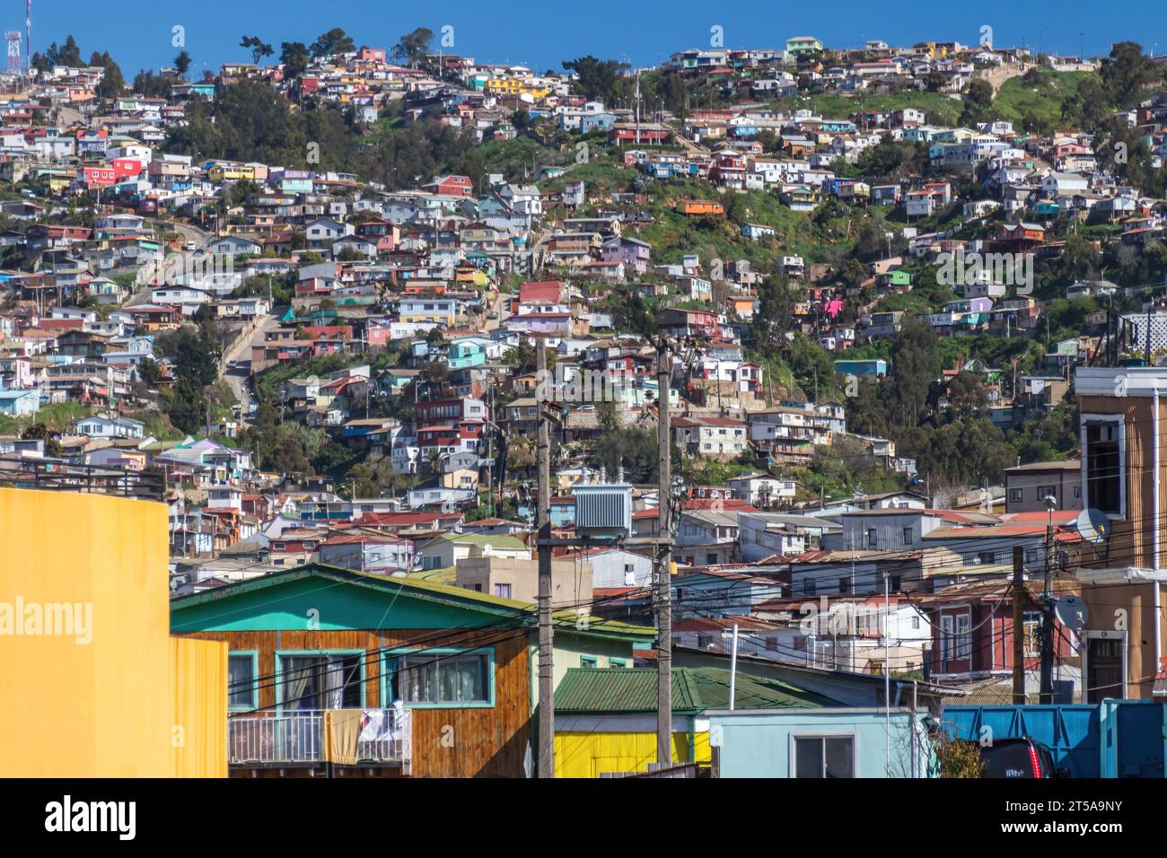 Buntes Stadtbild mit Häusern in Valparaiso, Chile. Die Gebäude sind eng zusammengesetzt und breiten sich in der Wintersonne den Hang hinauf aus. Stockfoto