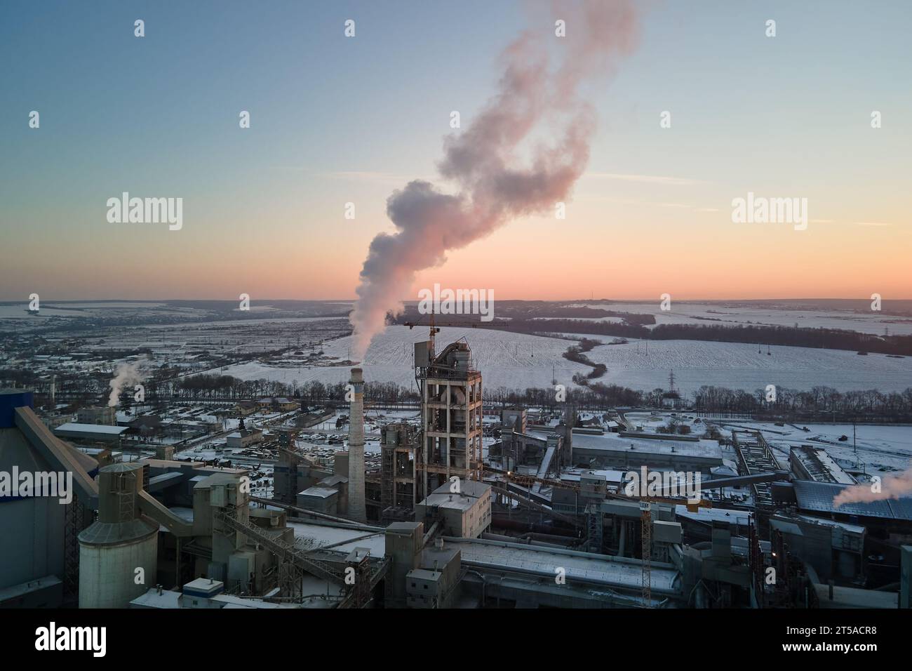 Luftaufnahme des Produktionsbereichs der Zementfabrik mit hoher Betonwerkstruktur und Turmdrehkranen am Industriestandort. Treibhausgase rauchbelastend Stockfoto