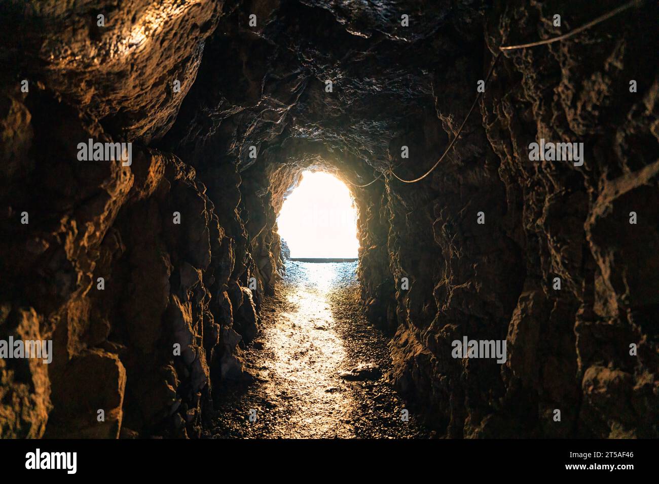 Natürlicher Höhlenbergbau unterirdischer Tunnelfelsen und goldenes Licht am Ziel. Glaubenskonzept über Religion und Gott Stockfoto