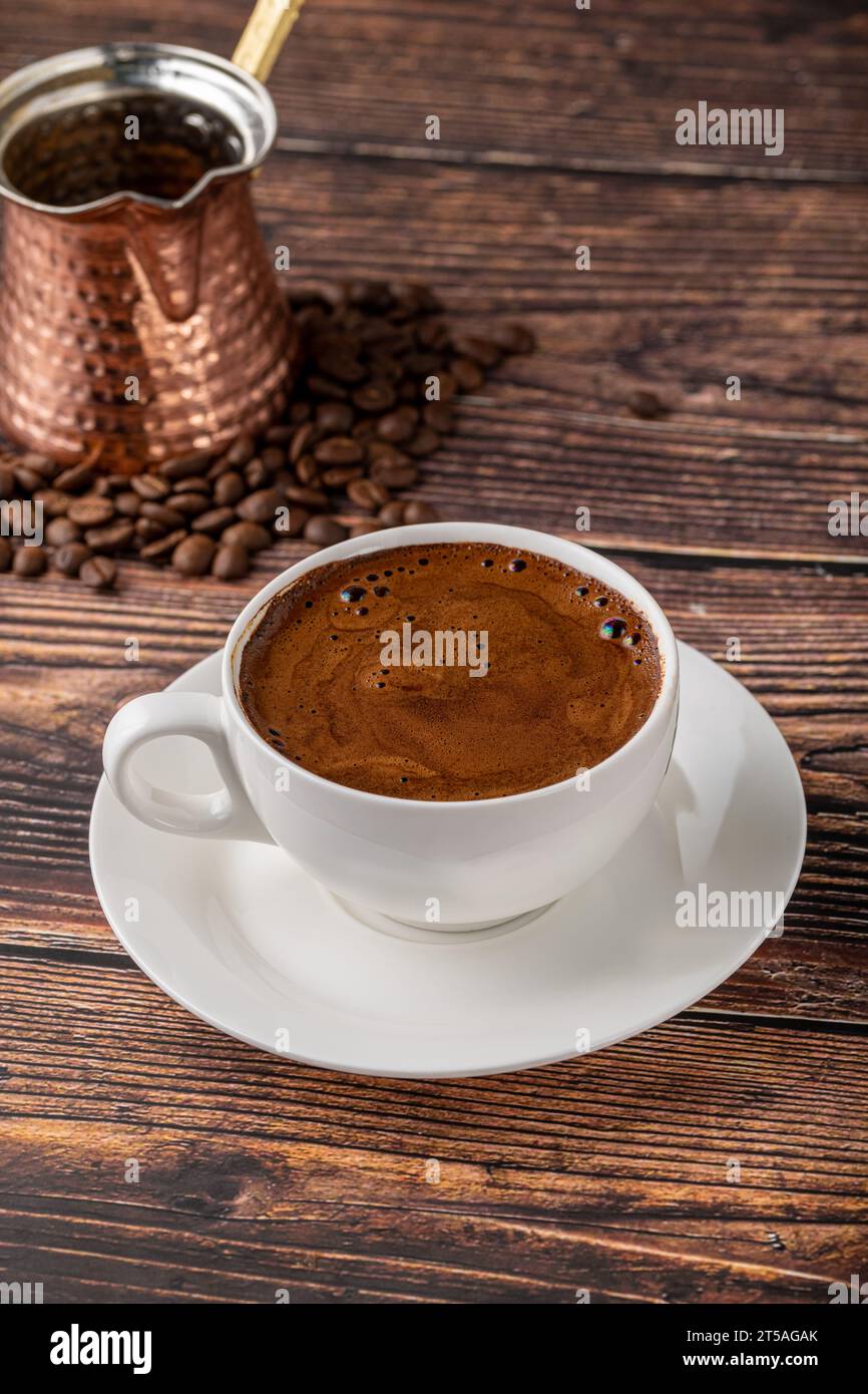 Doppelter türkischer Kaffee in einer weißen Porzellantasse mit dekorativer Kaffeekanne auf einem Holztisch Stockfoto