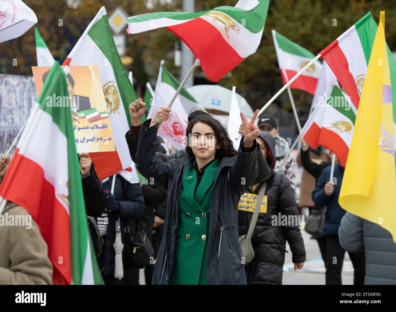 Genf, Schweiz. November 2023. Eine junge Frau zeigt ein Zeichen des Sieges, während sie von Fahnen der ursprünglichen dreifarbigen iranischen Flagge mit dem Aufdruck Löwe und Sonne während einer Kundgebung umgeben ist. Hunderte Anhänger des Nationalen Widerstandsrates des Iran (NCRI) nehmen an einer Kundgebung im Palais des Nations vor dem Europäischen Hauptquartier der Vereinten Nationen Teil, um gegen die Ernennung des iranischen Regimegesandten zum Vorsitzenden des Sozialforums des UN-Menschenrechtsrates zu protestieren. Quelle: SOPA Images Limited/Alamy Live News Stockfoto