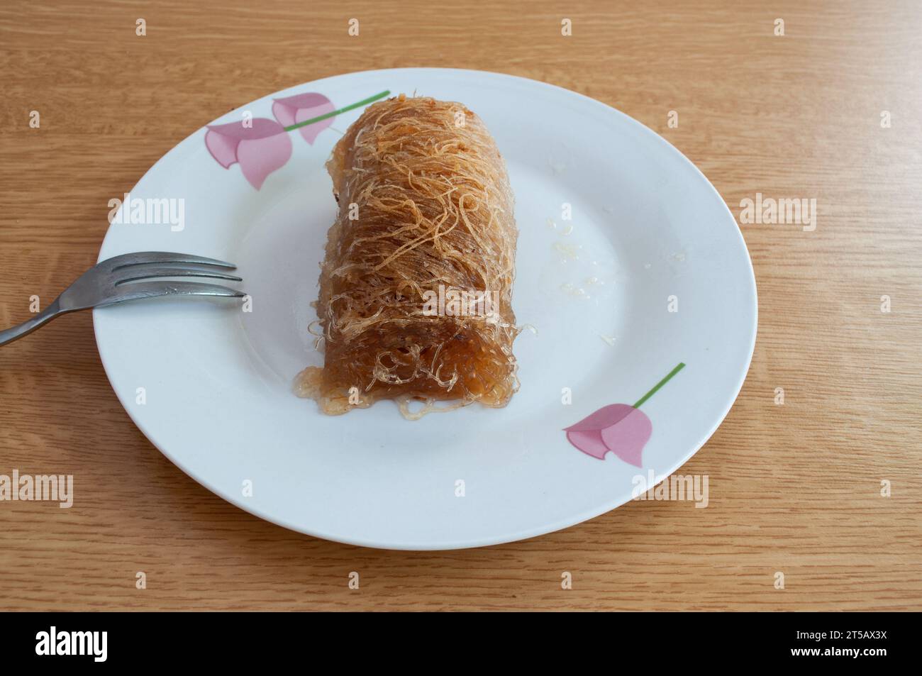 Griechische Küche: Köstliches Stück Kataifi-Dessert auf einem Blumenteller mit Gabel Stockfoto