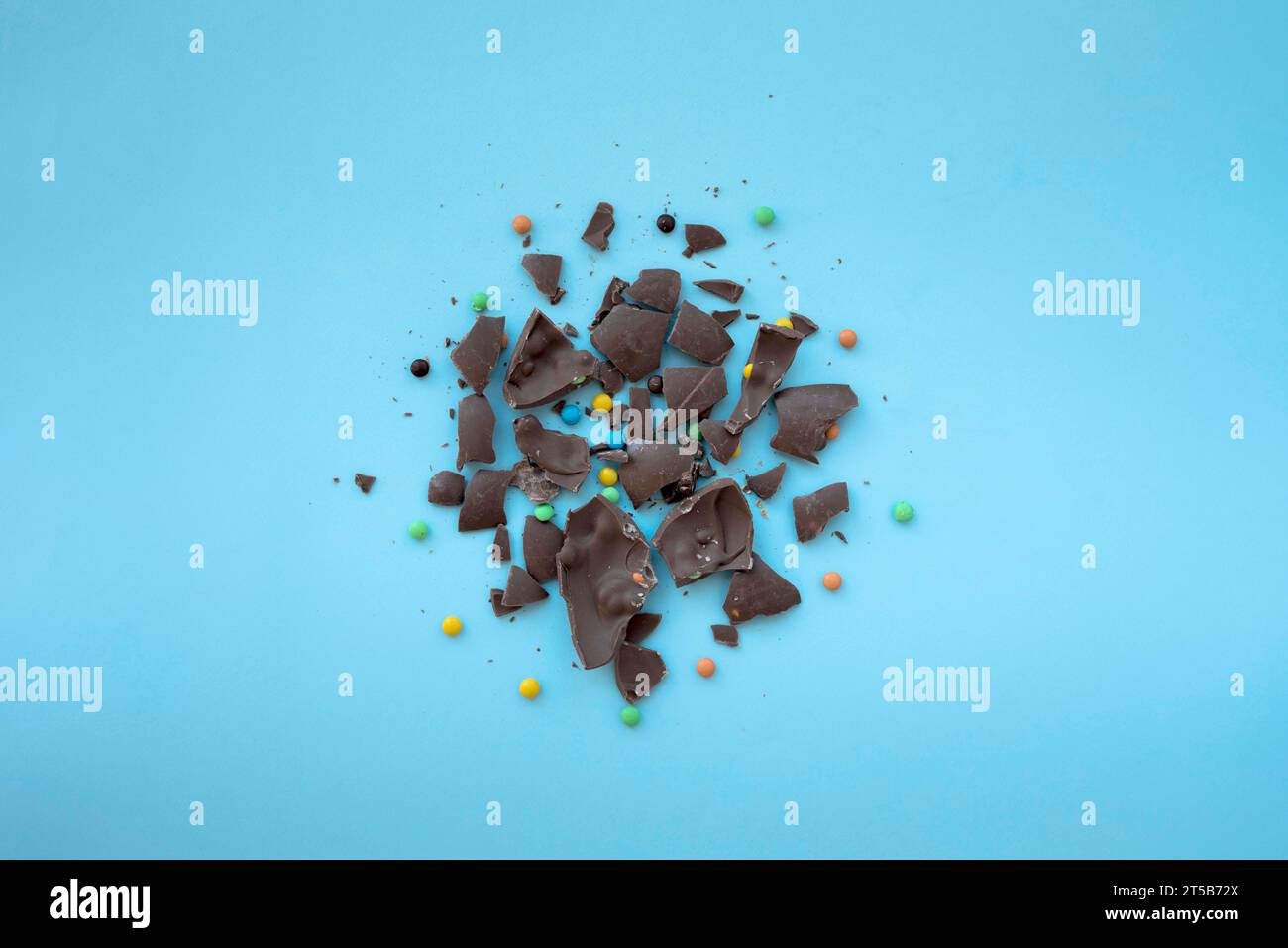 Zerbrochene Schokolade mit kleinen Süßigkeiten, blauem Tisch Stockfoto
