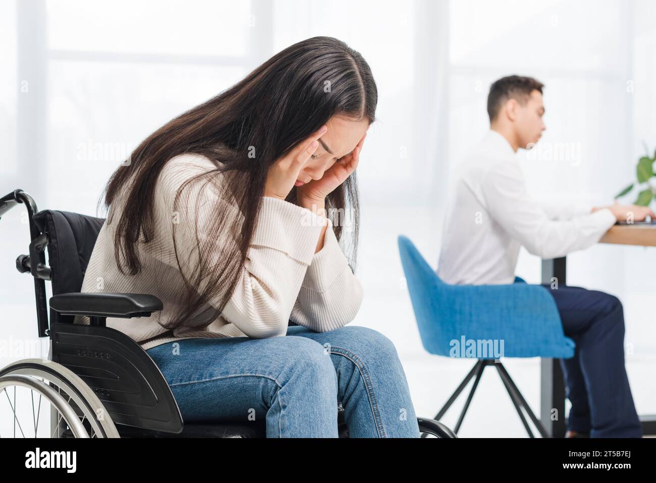 Frustrierte junge Frau mit Kopfschmerzen sitzender Rollstuhl-Geschäftsmann im Büro Stockfoto