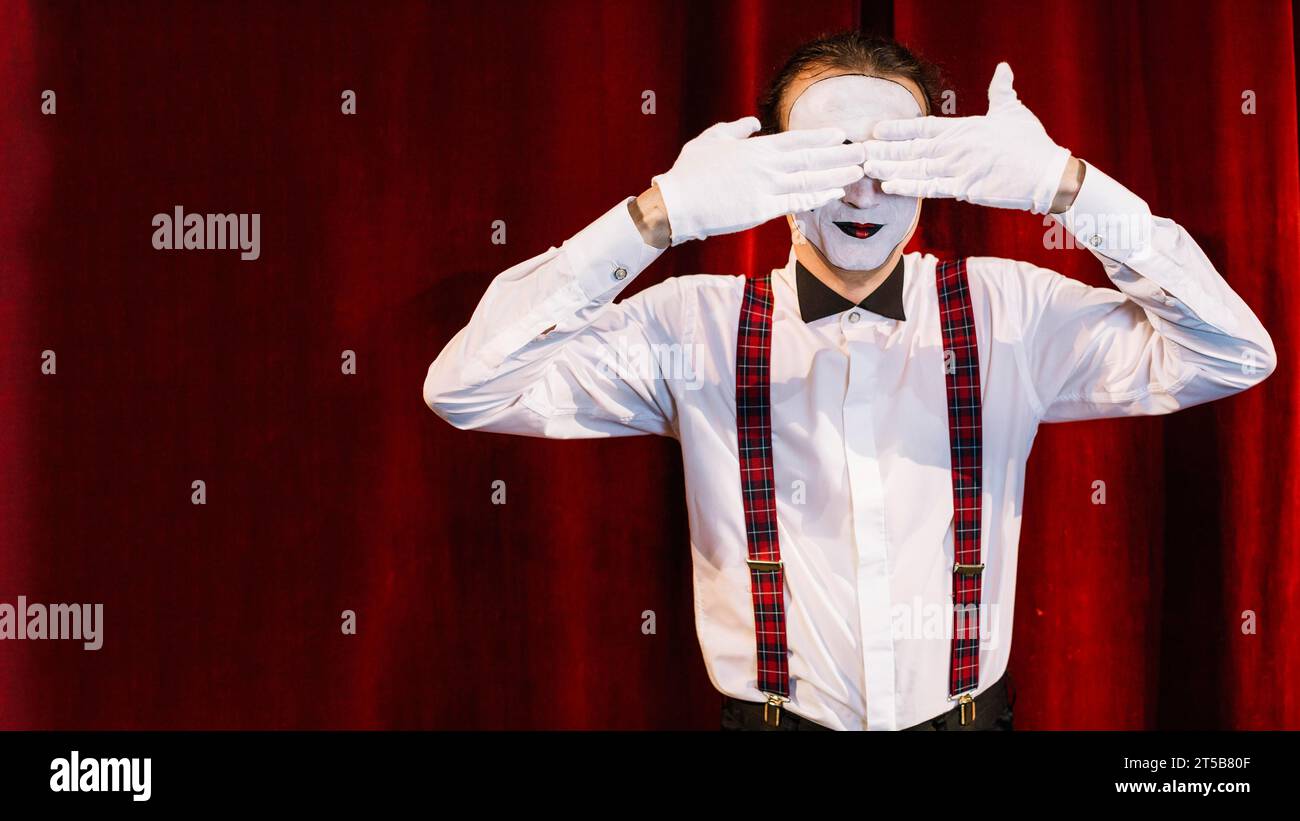 Ein männlicher Mime-Künstler steht vor dem Vorhang, der seine Augen mit Händen bedeckt Stockfoto
