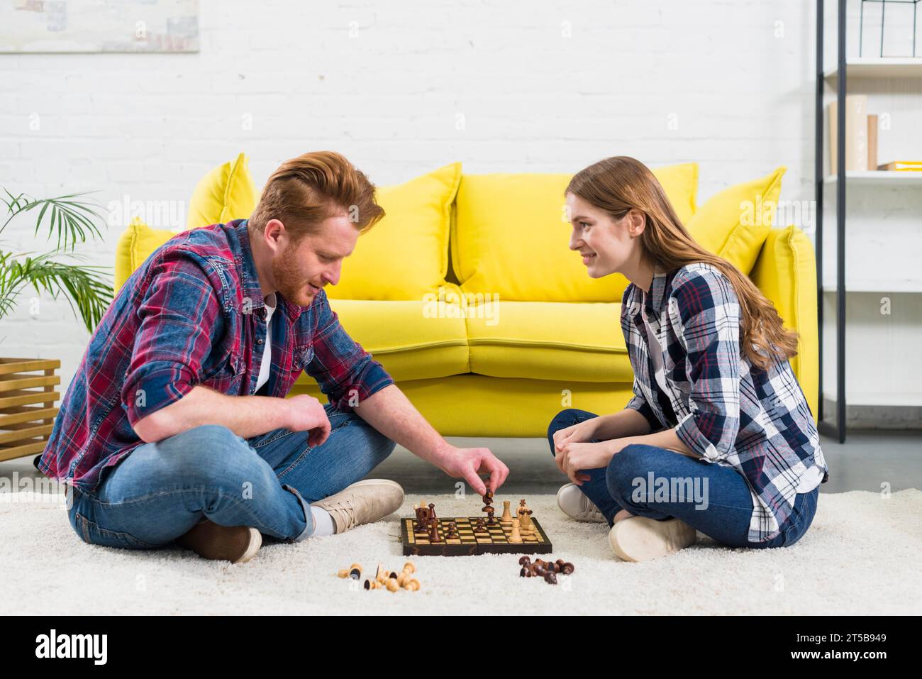 Junge Frau, die Mann aussieht, spielt Schachspiel im Wohnzimmer Stockfoto