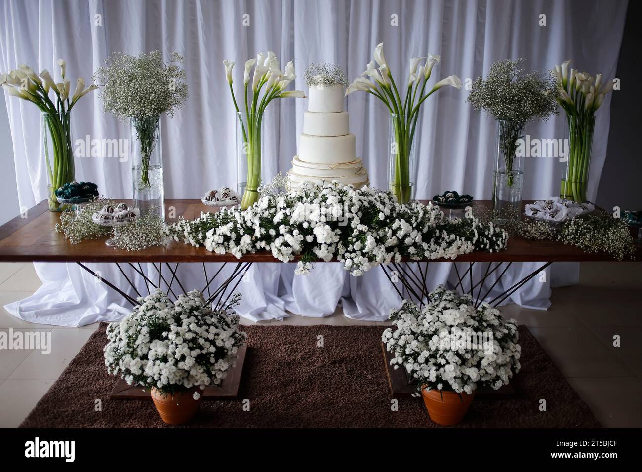 Hochzeitstisch: Eleganter weißer Tisch mit Kuchen und Blumen für Hochzeitsfeiern Stockfoto