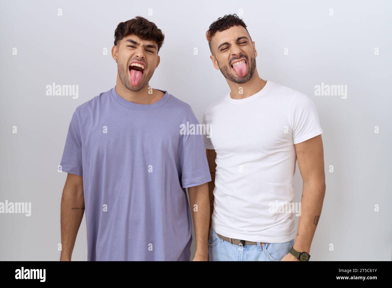Homosexuelles schwules Paar, das über weißem Hintergrund steht und die Zunge ausstreckt, glücklich mit lustigem Ausdruck. Emotionskonzept. Stockfoto