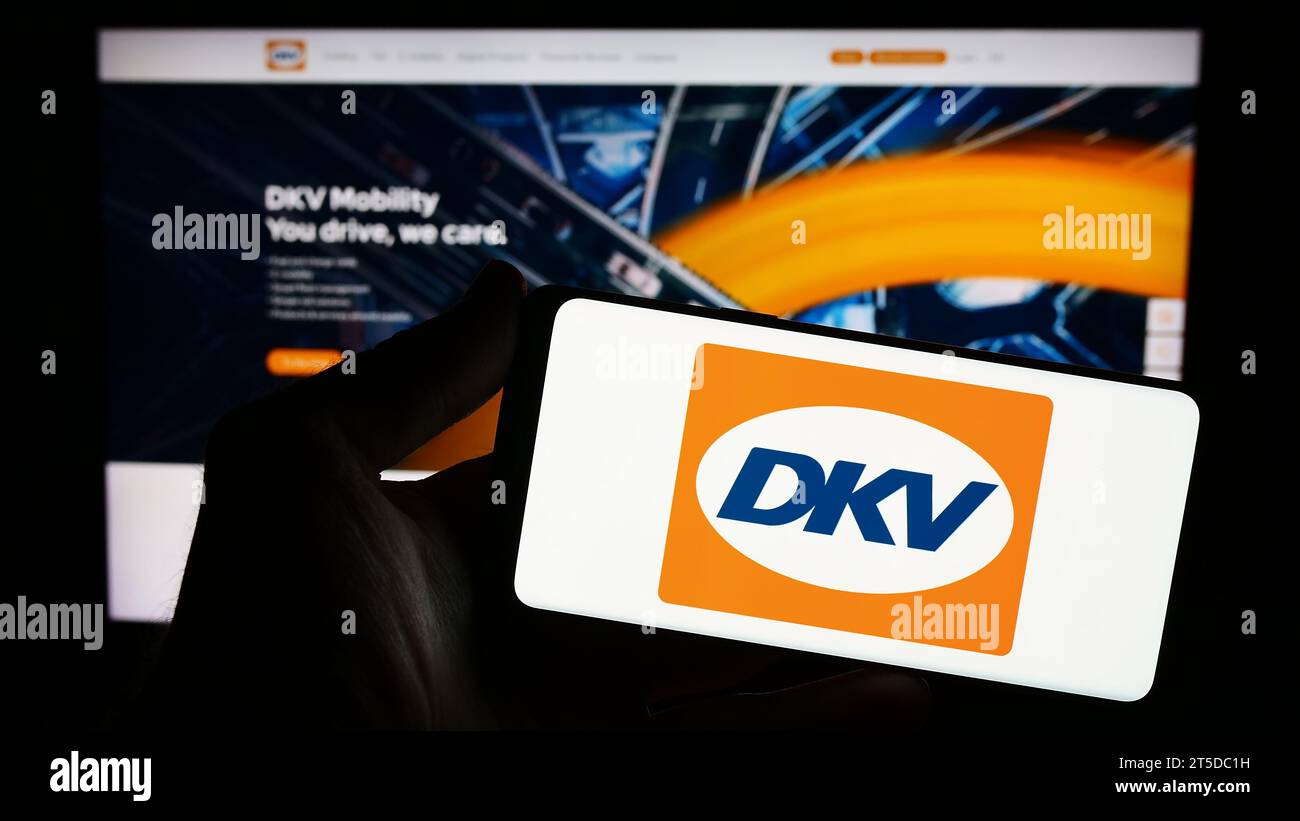 Person mit Smartphone mit Logo des deutschen B2B-Zahlungsunternehmens DKV Mobility vor der Website. Schwerpunkt auf dem Display des Telefons. Stockfoto