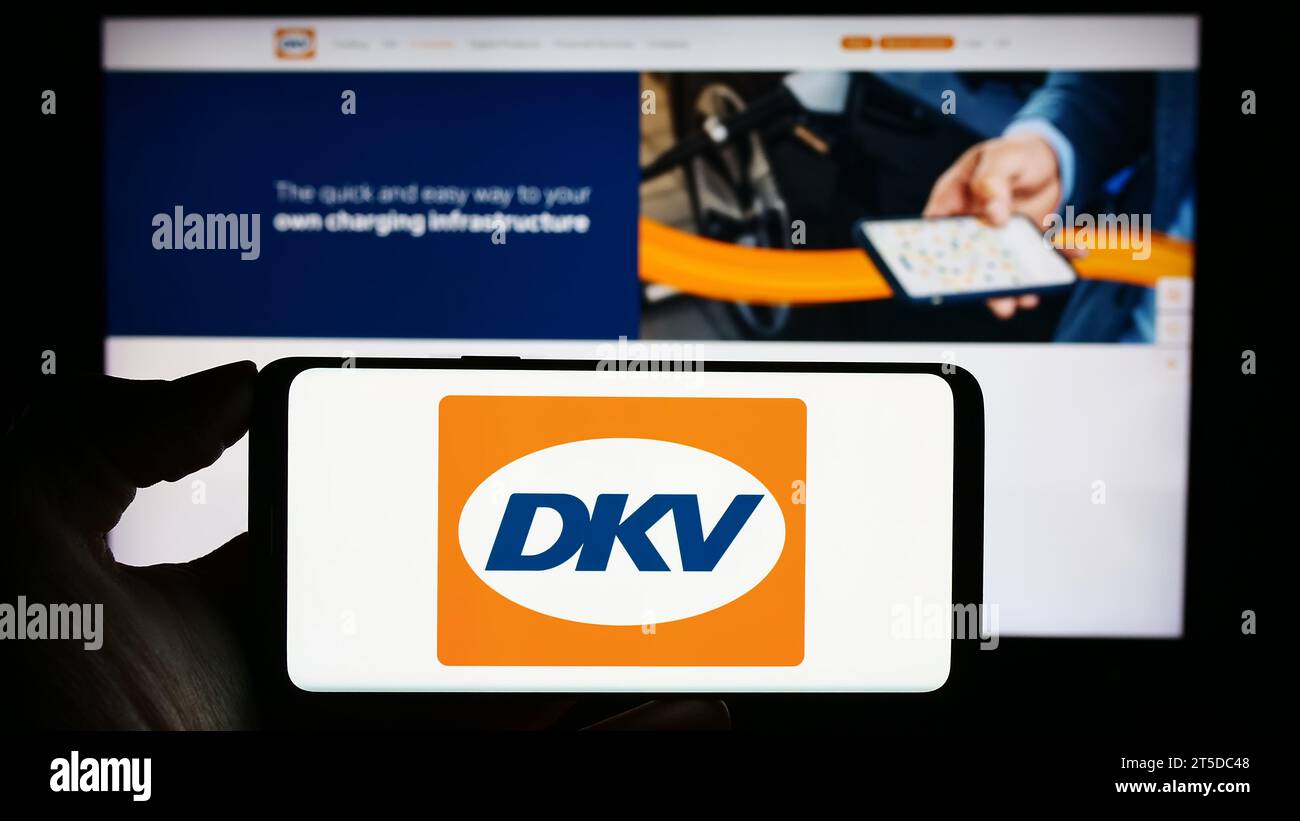 Person mit Mobiltelefon mit Logo des deutschen B2B-Zahlungsunternehmens DKV Mobility vor der Business-Webseite. Schwerpunkt auf dem Display des Telefons. Stockfoto