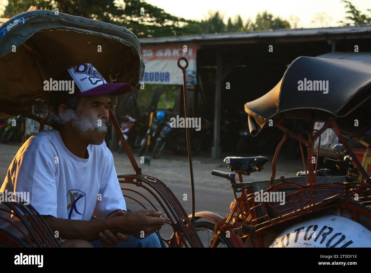 Ein indonesischer Rikscha-Fahrer raucht, während er auf einen Passagier wartet Stockfoto