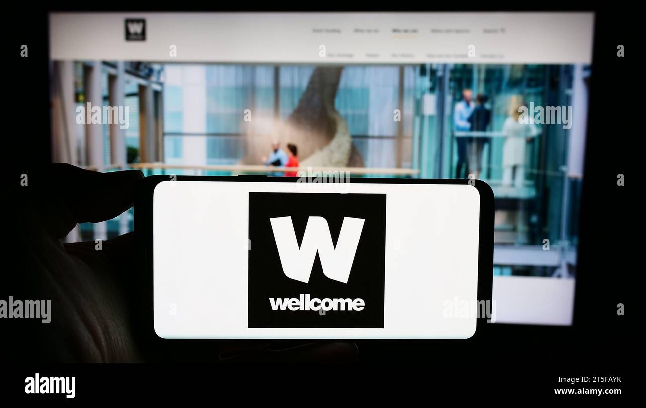 Person mit Smartphone und Logo der britischen Wohltätigkeitsstiftung Wellcome Trust vor der Website. Schwerpunkt auf dem Display des Telefons. Stockfoto