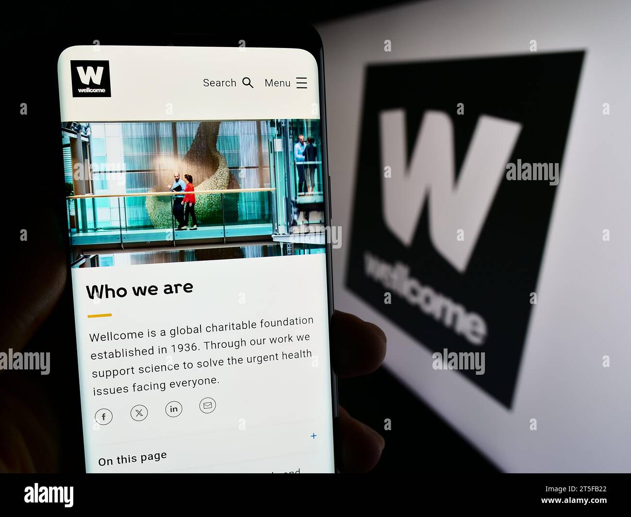 Person mit Mobiltelefon und Webseite der britischen Wohltätigkeitsstiftung Wellcome Trust vor dem Logo. Konzentrieren Sie sich auf die Mitte des Telefondisplays. Stockfoto