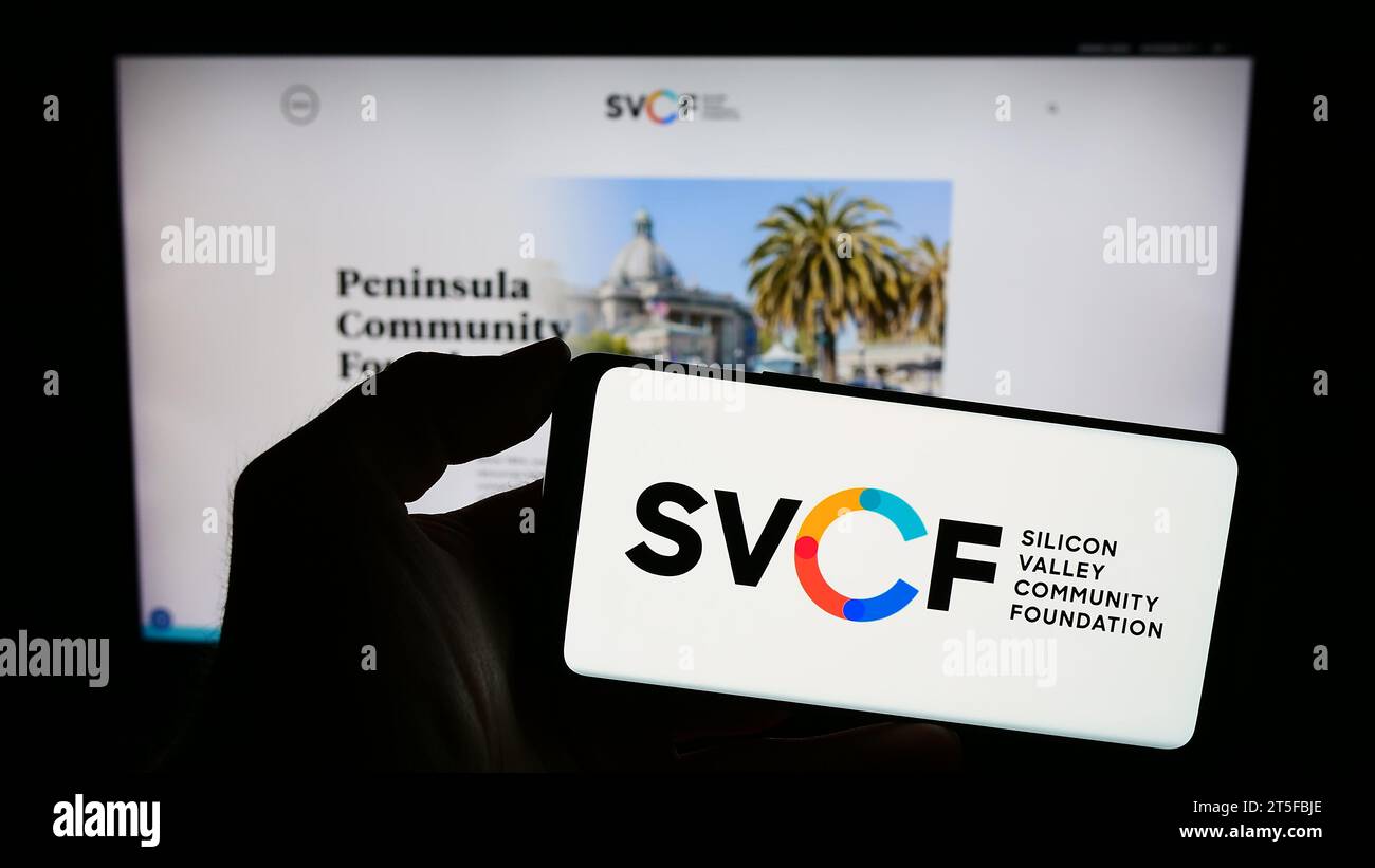 Person mit Mobiltelefon und Logo der US-Organisation Silicon Valley Community Foundation (SVCF) vor der Webseite. Schwerpunkt auf dem Display des Telefons. Stockfoto