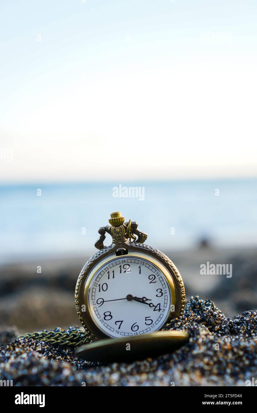 Eine goldene Taschenuhr ruht an Sandstränden, umrahmt von der sanften Kulisse der Strandwellen Stockfoto