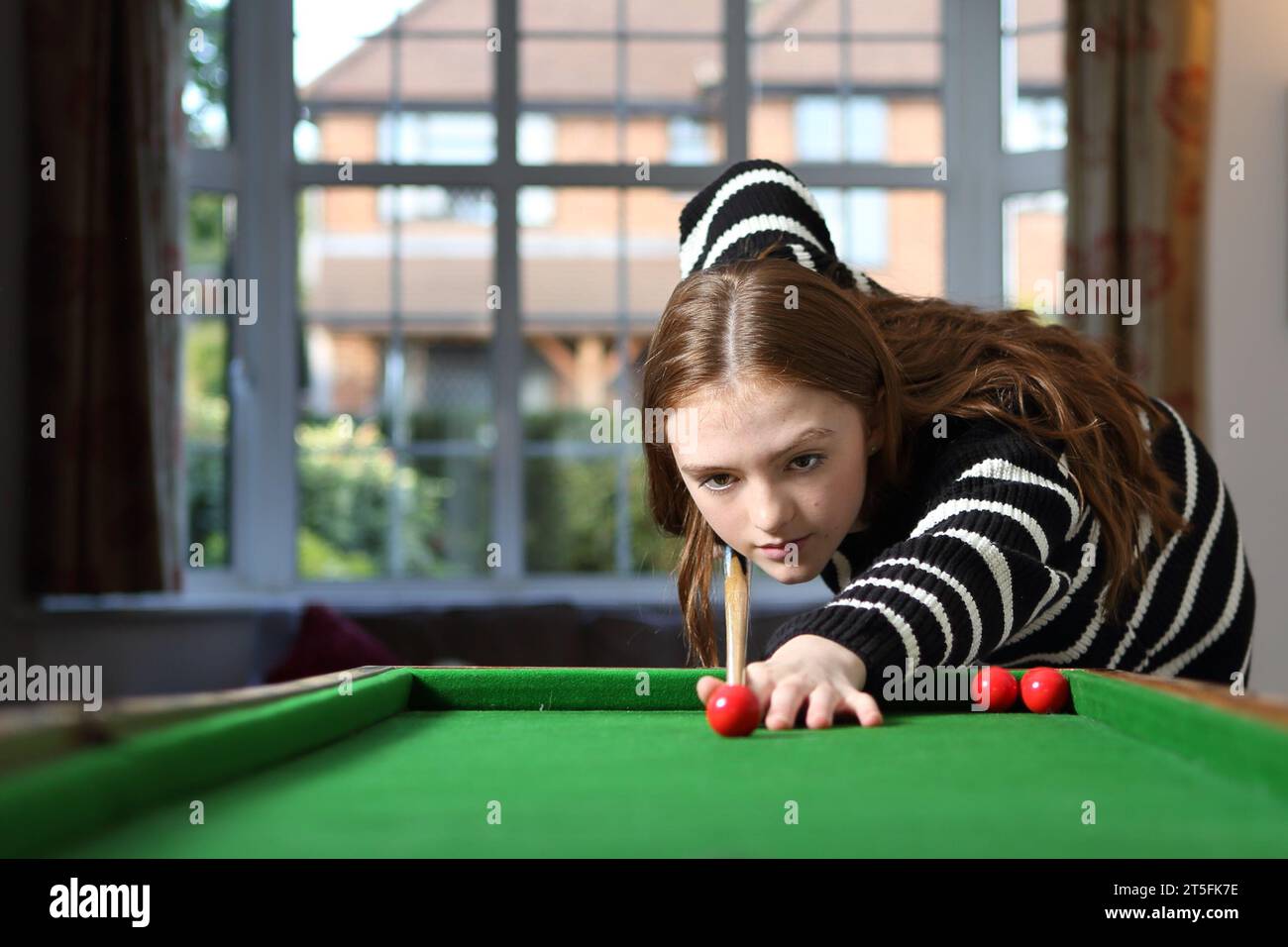 Teenager-Mädchen, das einen Schuss mit rotem Ball und Queue in einem Spiel Bagatelle anlegt Stockfoto