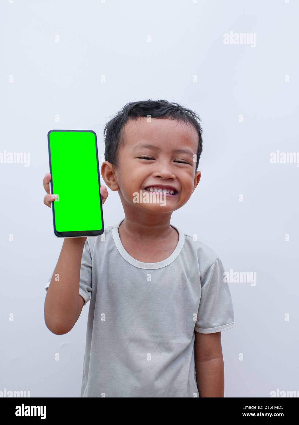 Kleiner asiatischer Junge, der ein Telefon in der Hand hält, mit einem grünen Bildschirm Stockfoto