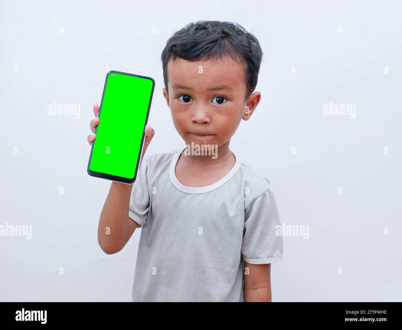 Kleiner asiatischer Junge, der ein Telefon in der Hand hält, mit einem grünen Bildschirm Stockfoto