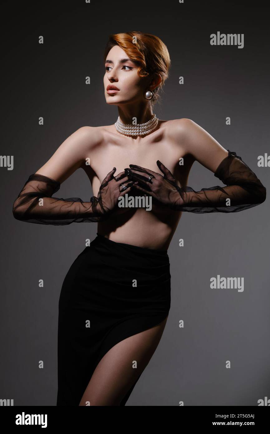 Schöne luxuriöse junge Frau mit sauberer Haut, die ihre nackte Brust bedeckt. Grauer Hintergrund im Studio. Stockfoto