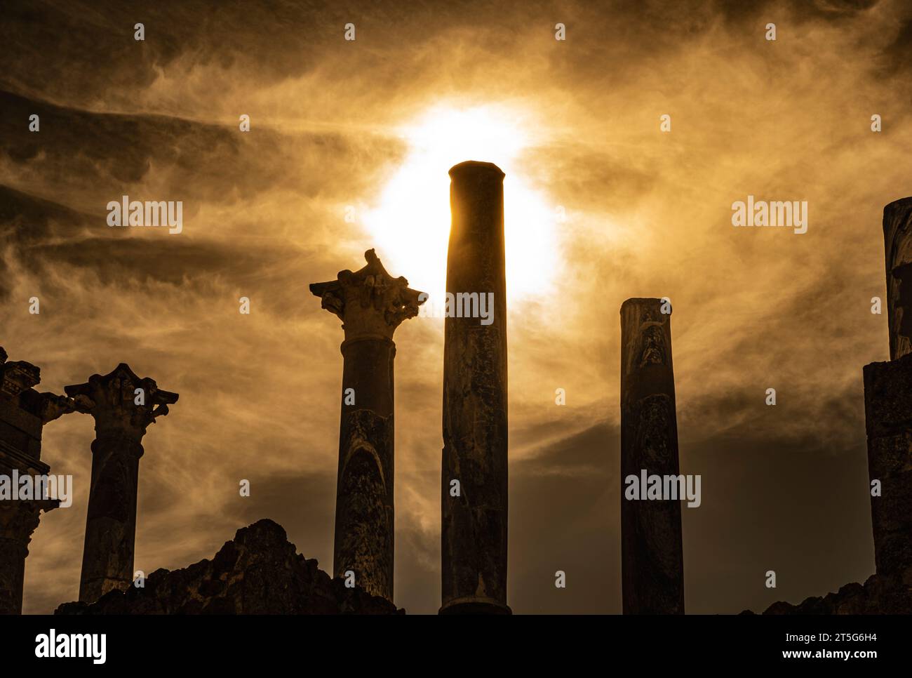Hintergrundbeleuchtete Details der Kapitelle und Säulen des römischen Theaters von Mérida, wobei die Sonne in der Abenddämmerung mit einem göttlichen Blitz aus einer dramatischen Wolke leuchtet Stockfoto