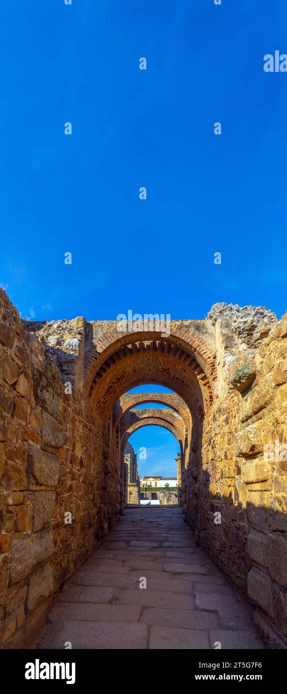 Restaurierte Bögen und Kopfsteinpflasterboden des archäologischen Komplexes Mérida mit den Häusern des Stadtzentrums von Mérida im Hintergrund beleuchtet von Stockfoto