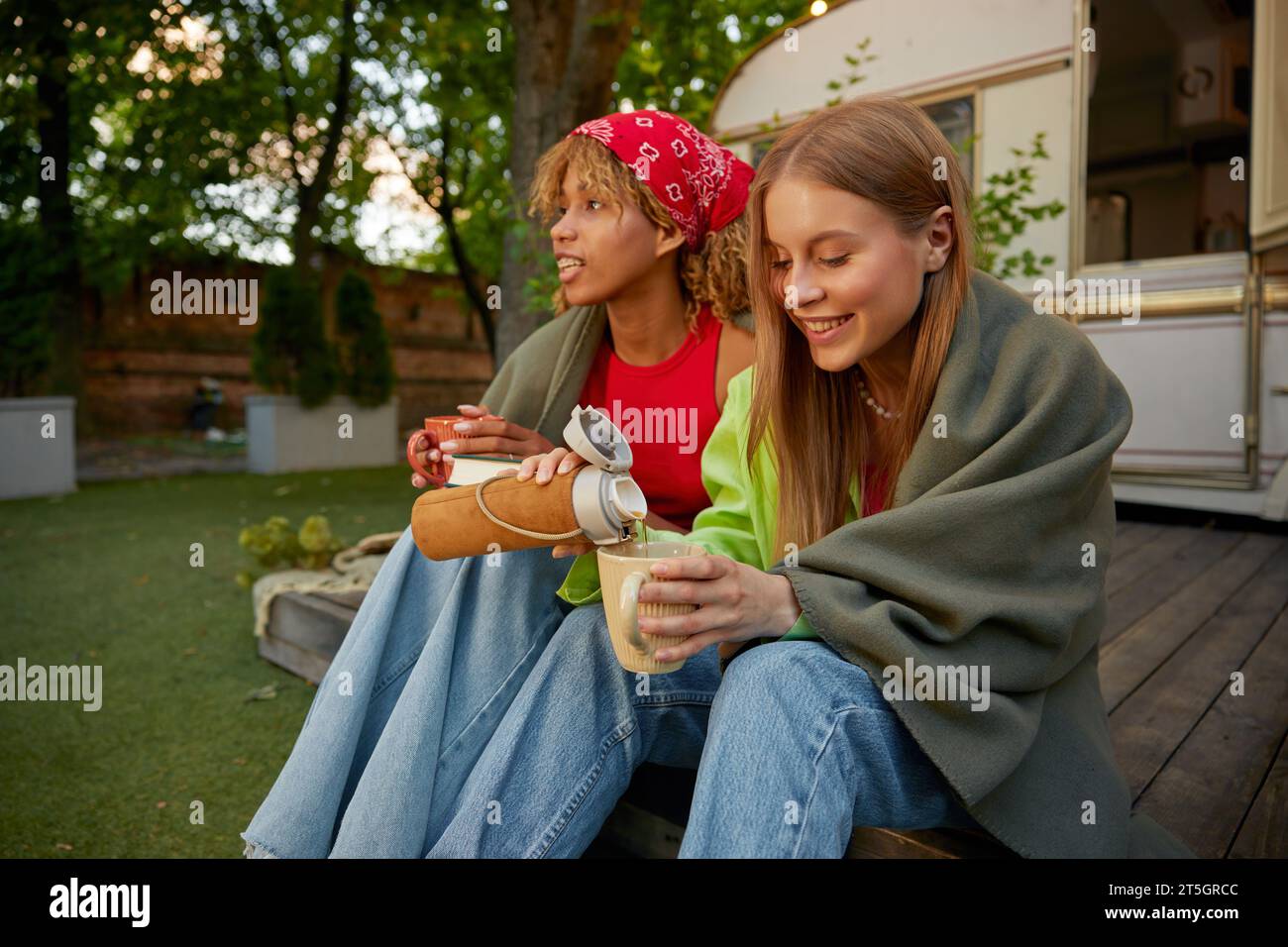 Zwei attraktive Freundinnen trinken heißen Tee und genießen Sommercamping-Vibes Stockfoto