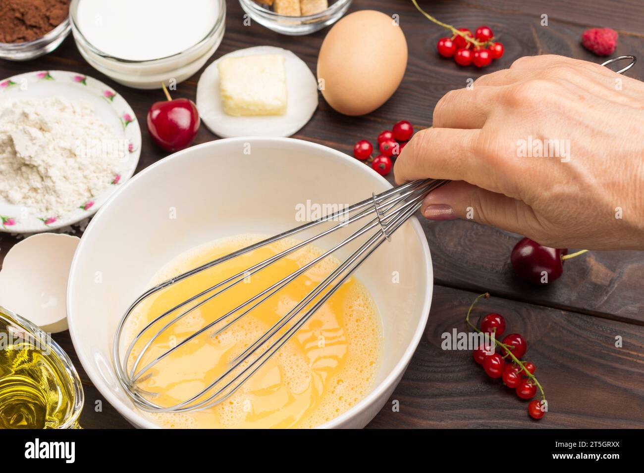 Die Eier in einer Schüssel mit dem Schneebesen von Hand verquirlen. Mehl, Milch, Beeren Zutaten zum Kochen des Frühstücks. Nahaufnahme. Stockfoto