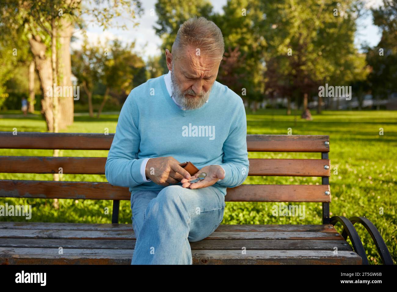 Konzentrierter Senior-Mann, der Münzen aus seiner Brieftasche zählt, während er auf der Bank sitzt Stockfoto