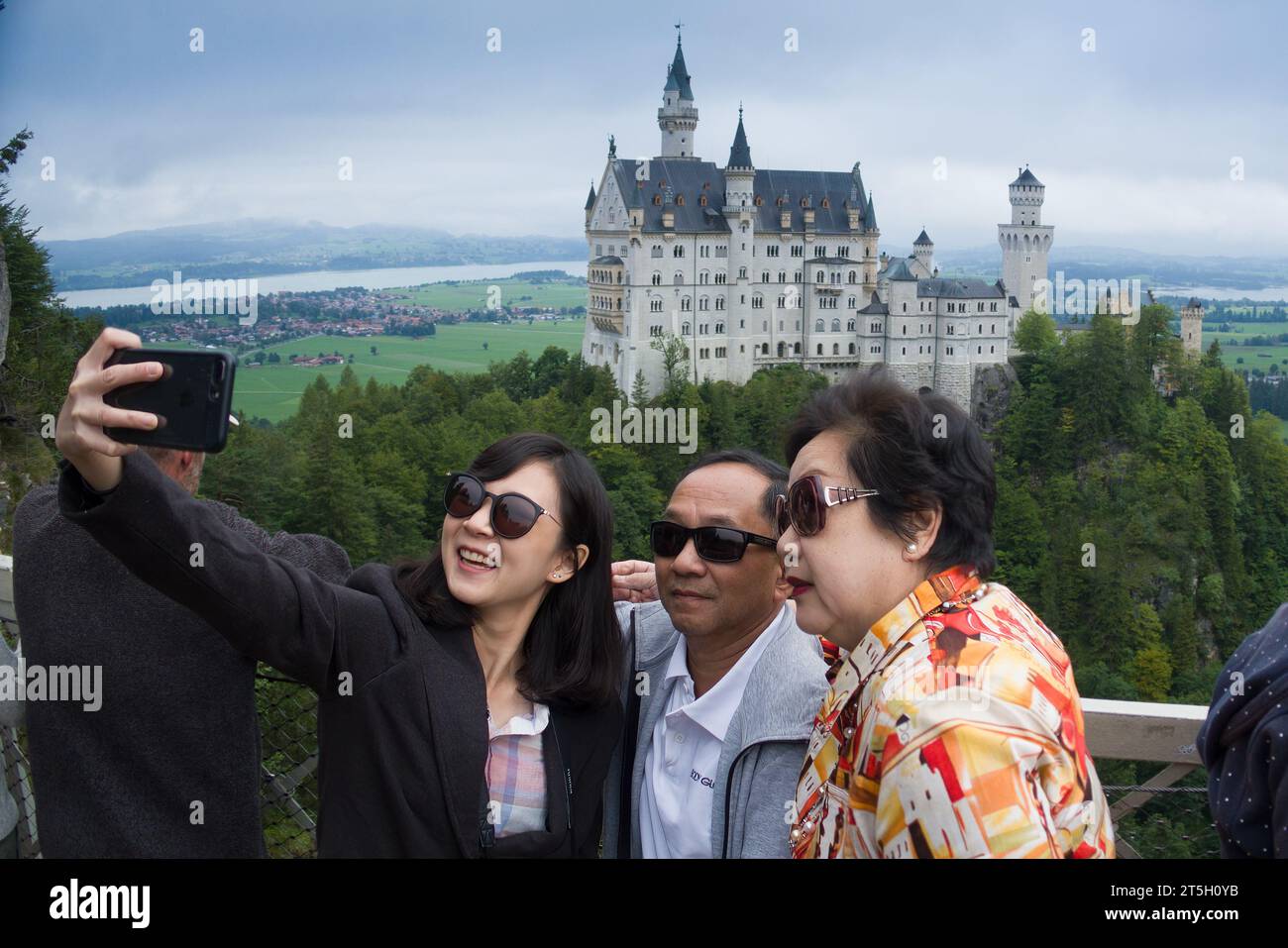 23. August 2019, Schwangau, Deutschland - glückliche asiatische Familie macht Selfies auf der Marienbrücke vor Schloss Neuschwanstein Stockfoto