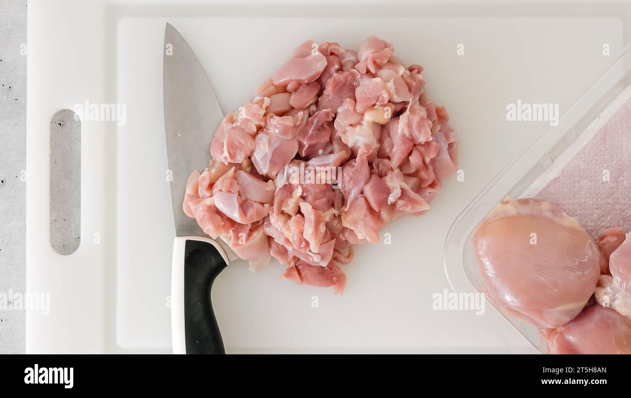 Gehacktes rohes Hähnchenfilet in Nahaufnahme auf einem weißen Plastikschneidebrett auf dem Küchentisch Stockfoto