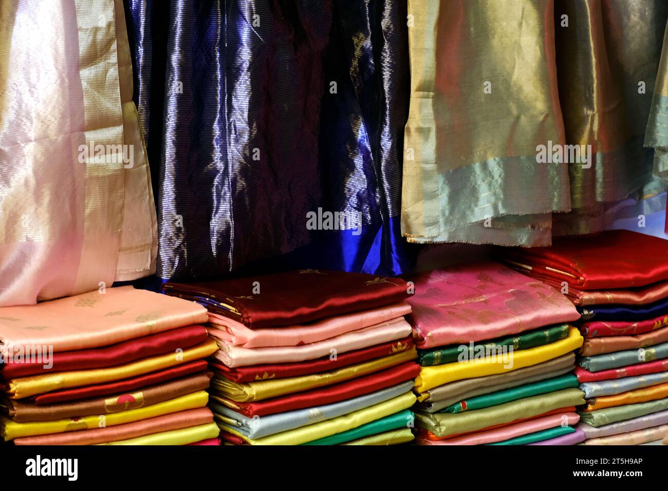 Schicke indische Sarees, fein säuberlich gestapelte bunte Seidensaris in Regalen in einem Textilgeschäft. Unglaubliches Indien. Stockfoto