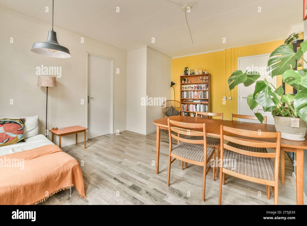 Ein Wohnzimmer mit gelben Wänden und Holzfußboden, darunter ein kleiner Esstisch, der von zwei Holzstühlen umgeben ist Stockfoto