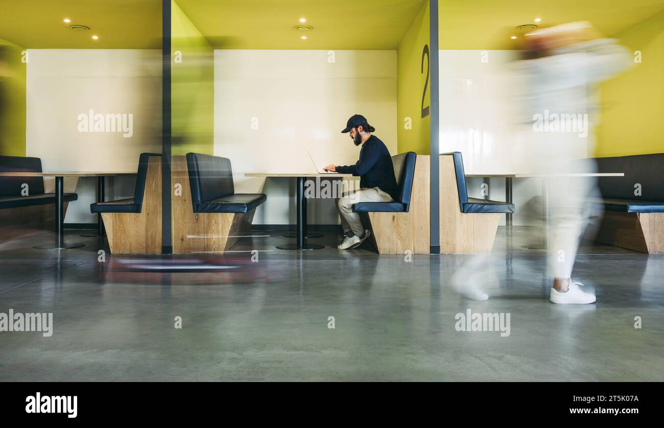 Softwareentwickler arbeiten an seinem Laptop in einem geschäftigen Coworking-Büro. Umgeben von Geschäftsleuten konzentriert er sich auf Programmierung und Programmierung in seinem Stand. V Stockfoto