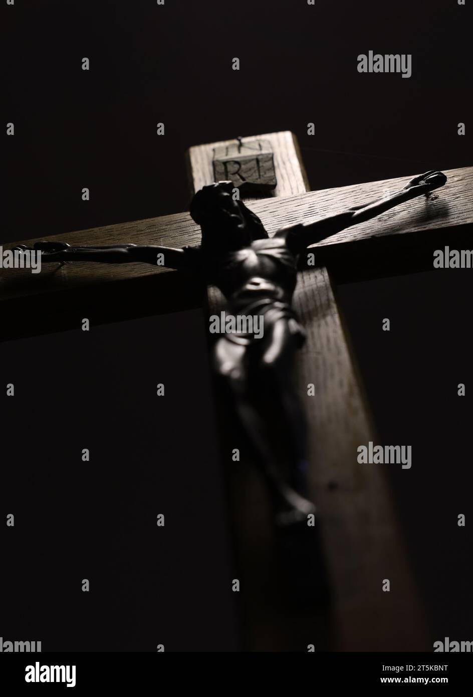 Jesus am Kreuz, der auf seine Anhänger herabblickt. Die Kreuzigung. Eine dunkle Silhouette auf einem Holzkreuz mit schwarzem Hintergrund Stockfoto