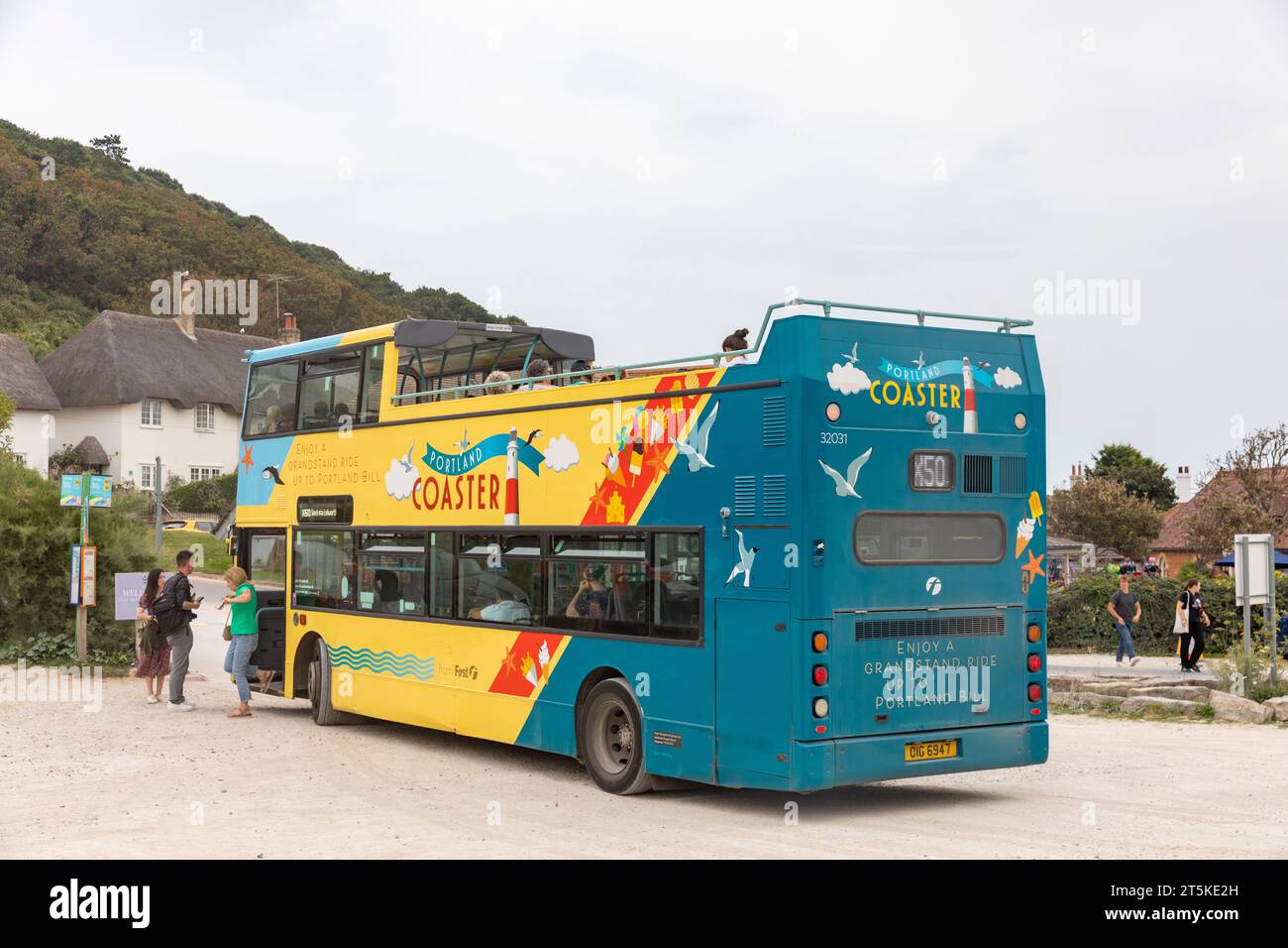 Portland Coaster Tour Bus mit offenem Oberdeck an der Jurassic Coast, der Touristen am Parkplatz der Lulworth Cove, Dorset, England, UK, 2023 abholt Stockfoto