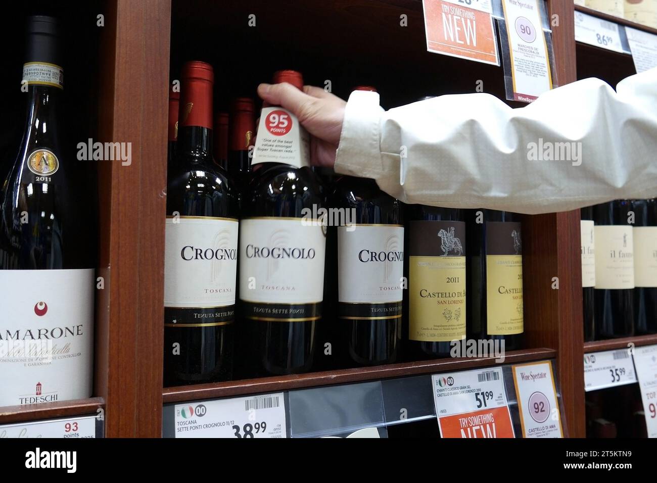 Eine Hand nimmt eine Flasche Rotwein aus dem Regal. Stockfoto